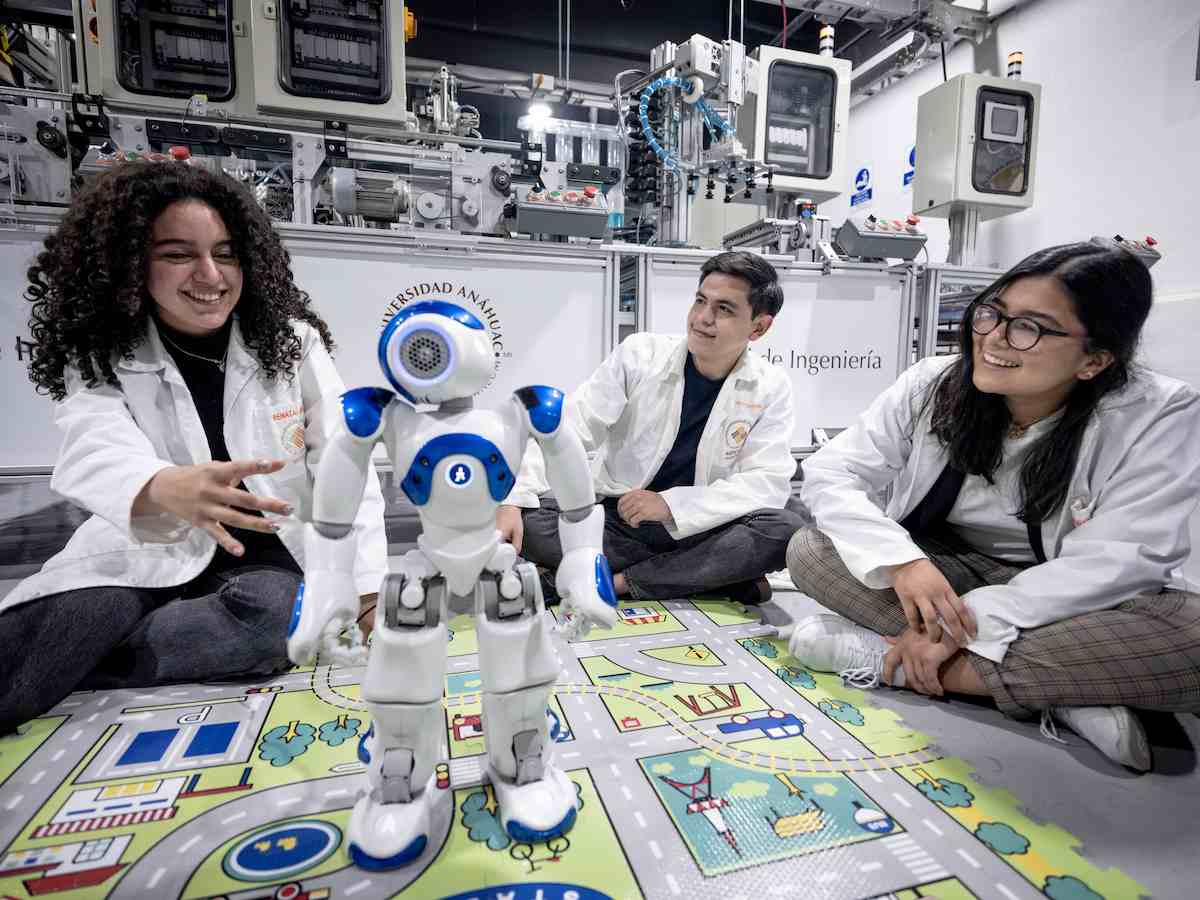 Estudiantes de ingeniería interactúan con un robot humanoide sobre tapete educativo en laboratorio de automatización.